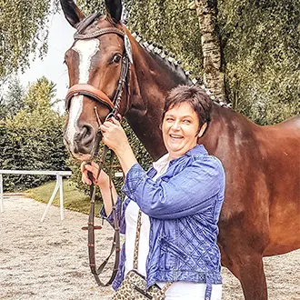 Frau steht neben Pferd und hält die Zügel.